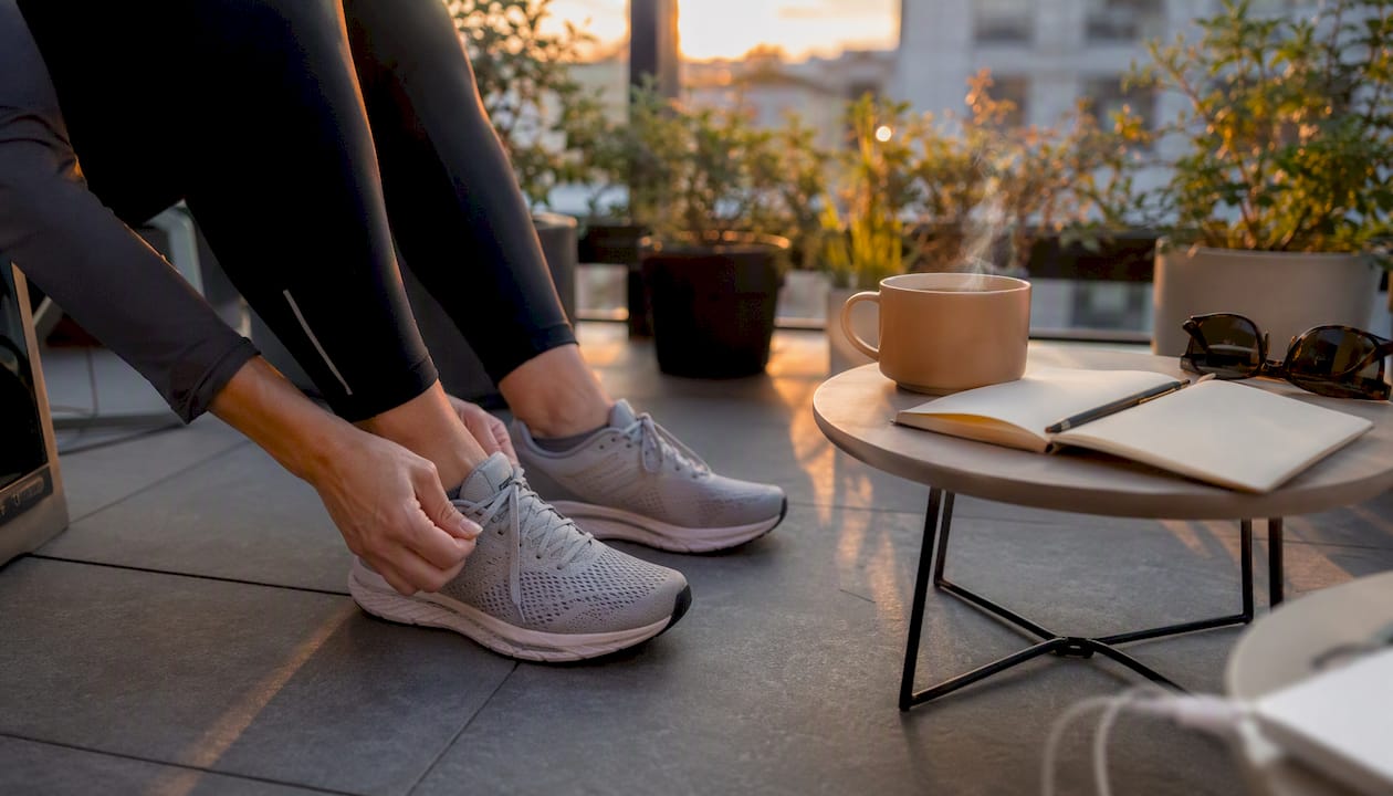 Hands tying running shoes with morning coffee nearby